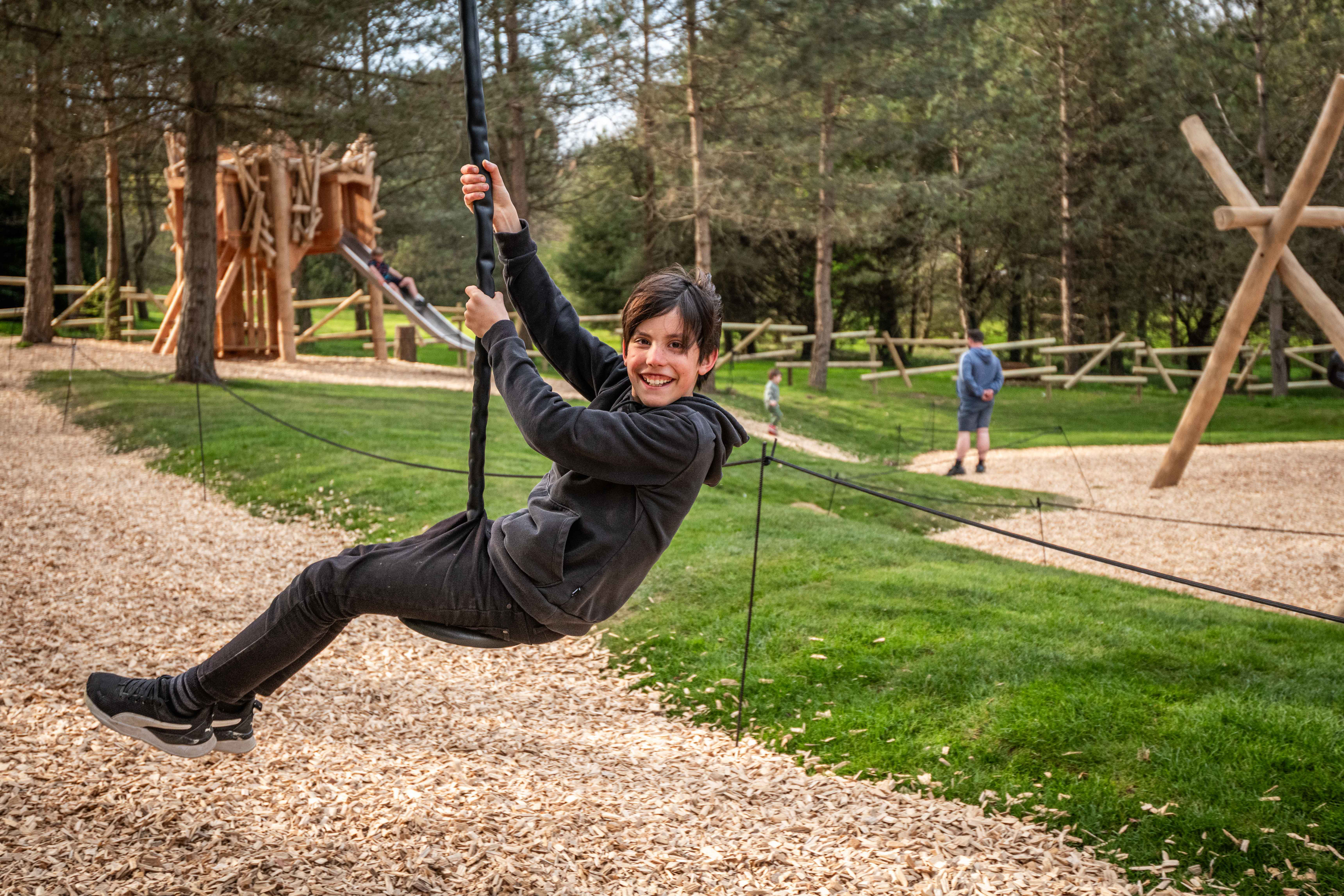 teen boy smiling whilst on zipline in forrest play ground