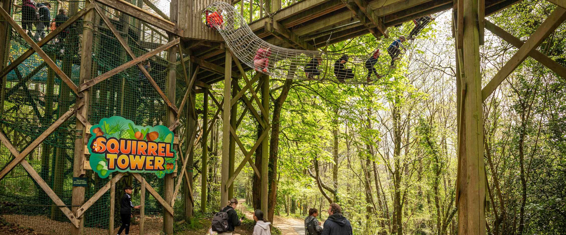 Children playing on wire tunnel with families watching