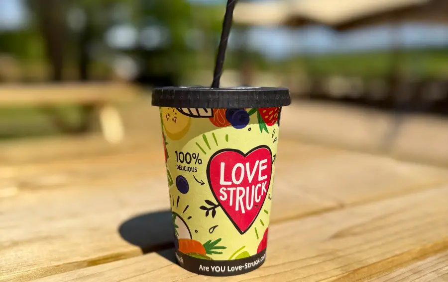 Bright and colourful paper smoothie cup with straw, pictured on a picnic bench in the sun