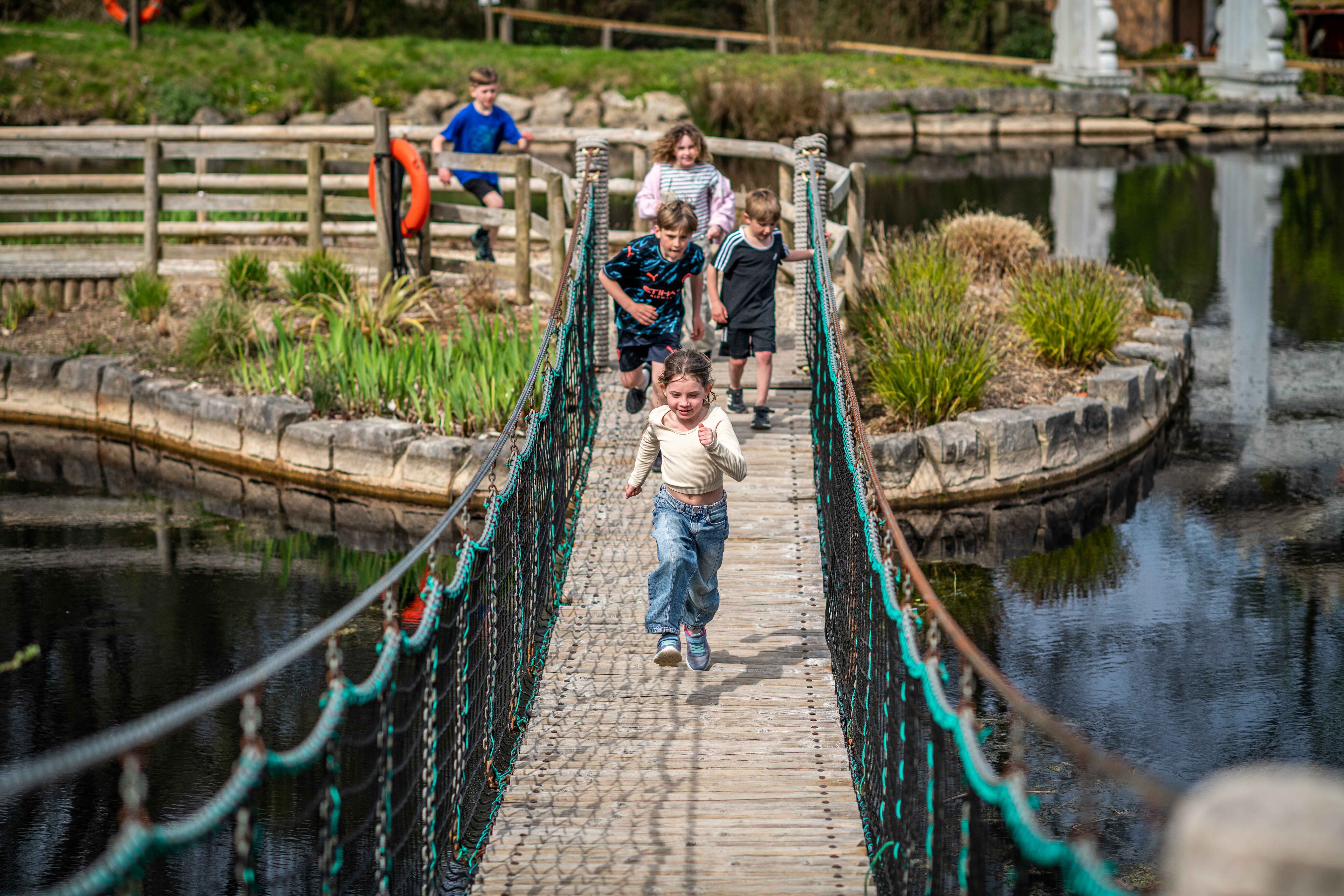 Children running across wobble bridges over pond