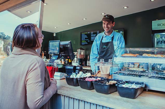 Male member of staff smiling whilst serving a lady at a cafe outlet