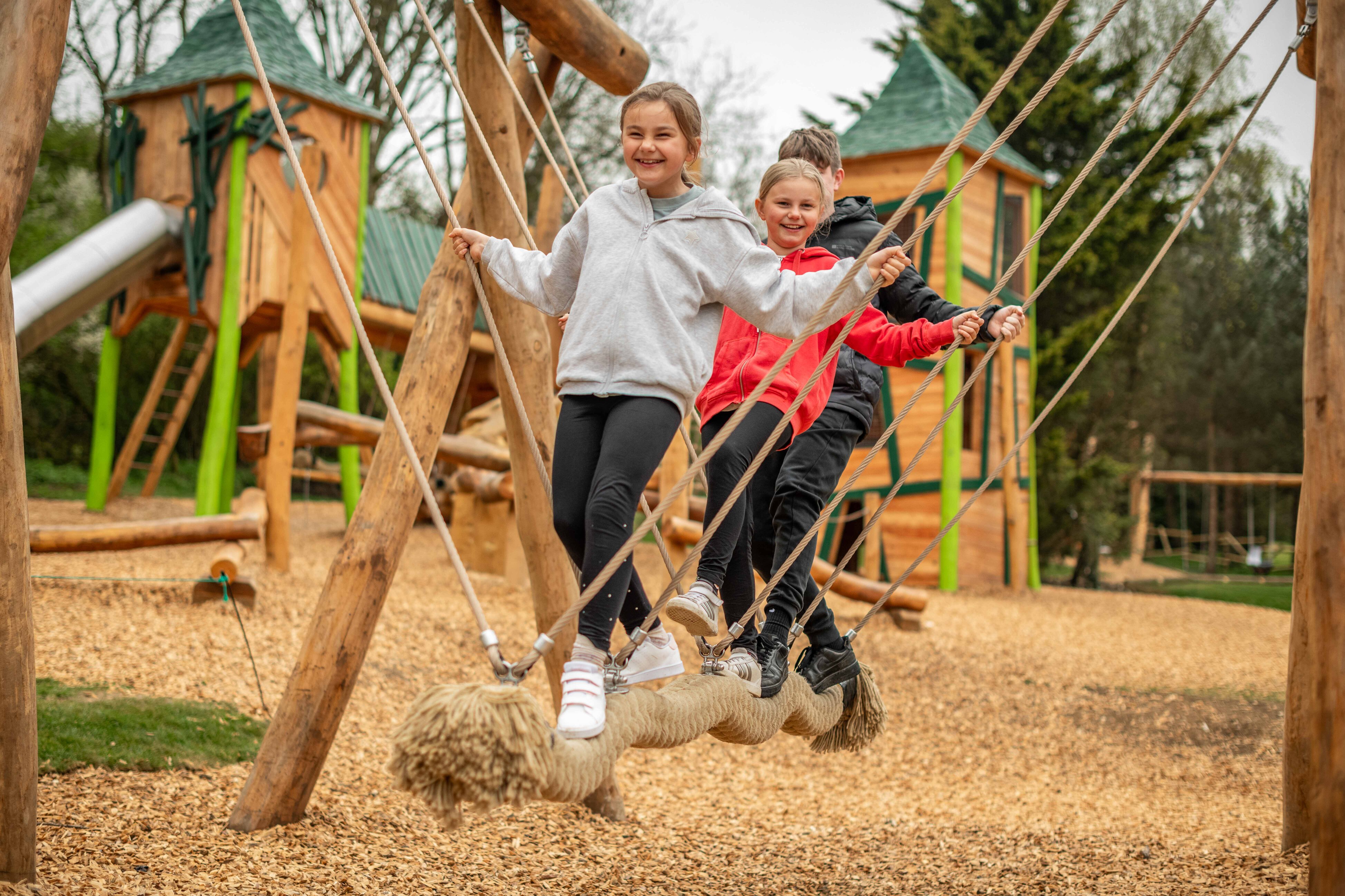Three children (two girls, one boy) playing on stand up swing at a large play area